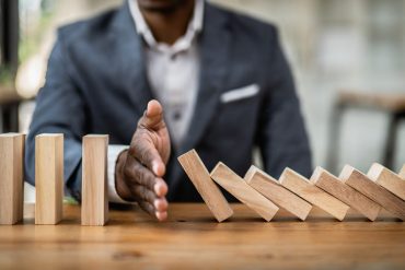 businessman-halts-falling-domino-with-hand-symbolic-control-preventing-chain-reaction
